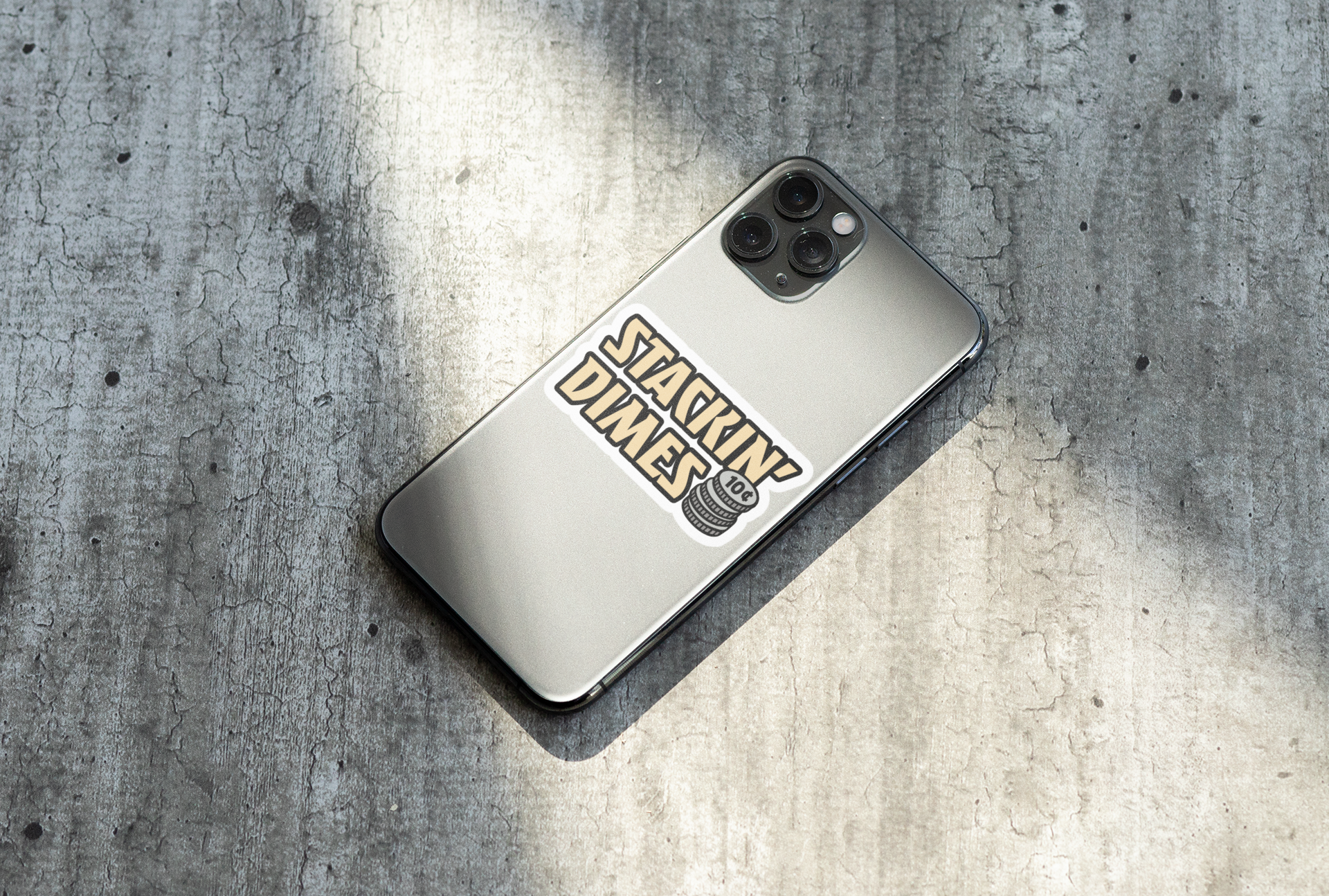 Phone case with 'Stackin Dimes' sticker on a concrete surface